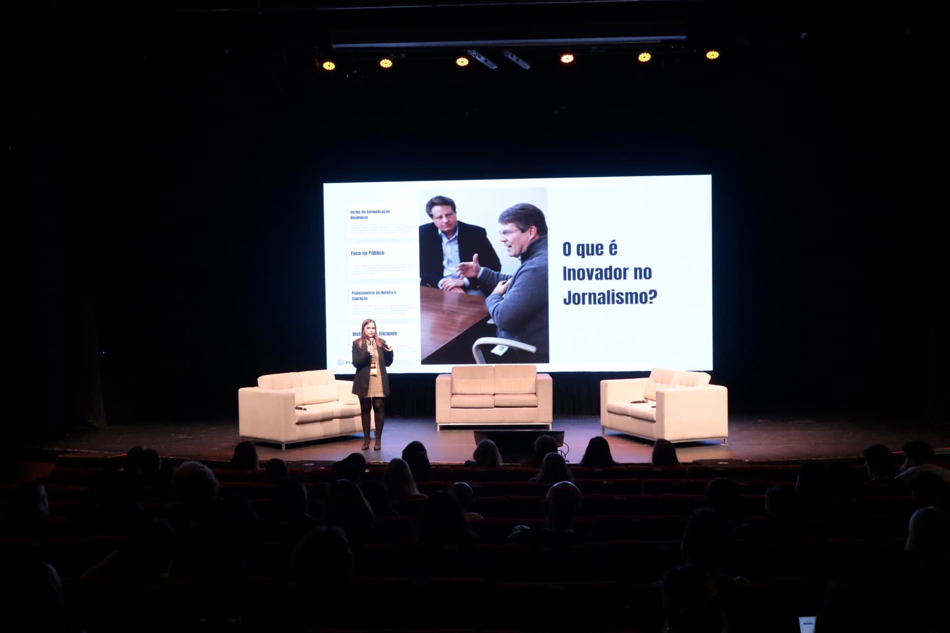 Palestrante no palco do Teatro Gazeta diante do telão com a pergunta O que é inovador no jornalismo